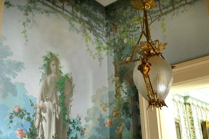 A corner of a room with a detailed wall mural and an ornate hanging lamp.